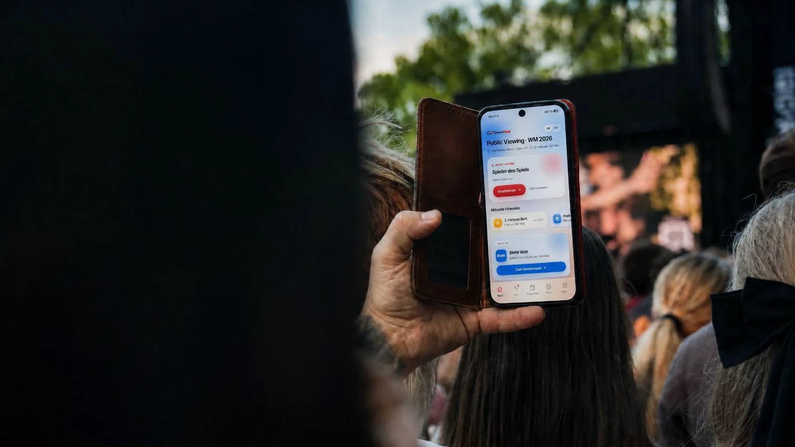 A fan in the crowd holds up a phone showing CrowdPortal with a vote and a sponsor notice